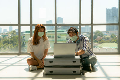 Man wearing mask using laptop at airport sitting by woman