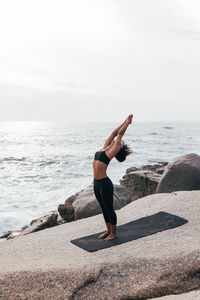 Full length of woman doing yoga at beach against sky