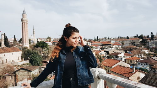 Young woman standing amidst buildings in town against sky