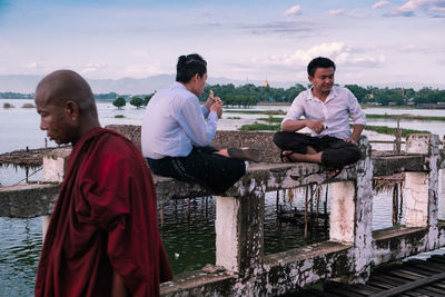 Men sitting by lake against sky