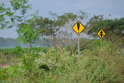 Road sign by trees on field against sky