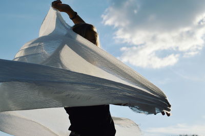 Woman holding scarf while standing against sky