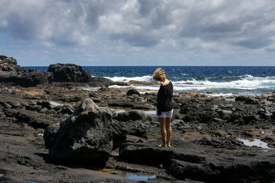 Full length of man standing on rock at beach against sky