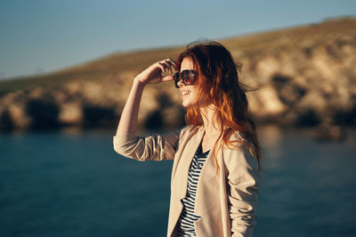 Woman wearing sunglasses standing against sea