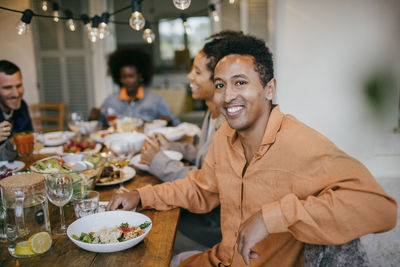 Portrait of happy man sitting at dining table during dinner party in patio