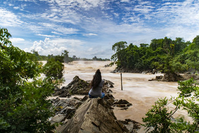 People sitting on rock by trees against sky