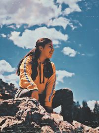 Woman sitting on rock against sky