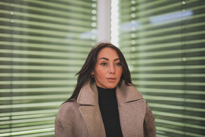 Portrait of young woman standing against window