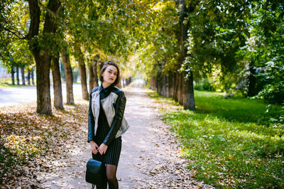 Portrait of young woman standing amidst trees at park