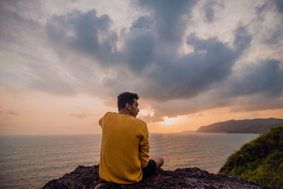 Rear view of woman looking at sea against sky during sunset