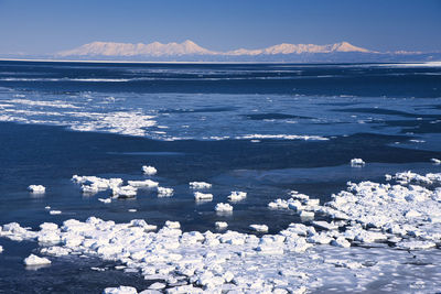 Scenic view of sea by snowcapped mountains against sky