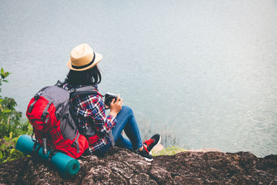 Rear view of men sitting on rock by lake