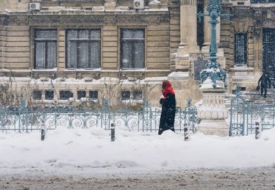 Side view of woman walking on snow covered footpath in city