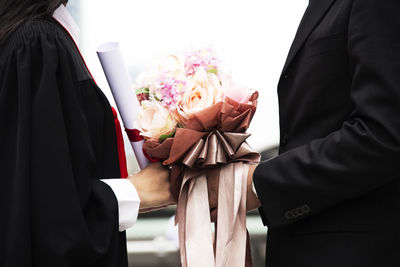 Midsection of businessman giving bouquet to student during graduation