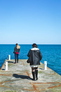 Rear view of people walking on pier against clear blue sky