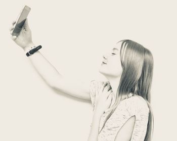 Smiling young woman taking selfie against white background