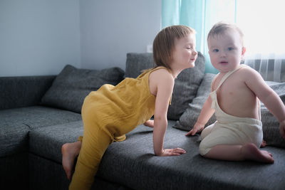 Kids brother 1 year old and sister 3 years old play together on couch in real living room