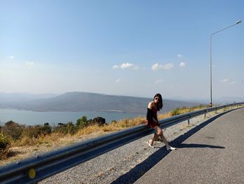 Young woman sitting on railing by road