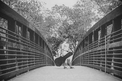 Man carrying guitar case on footbridge