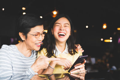 Mother and daughter laughing while holding mobile phone in restaurant