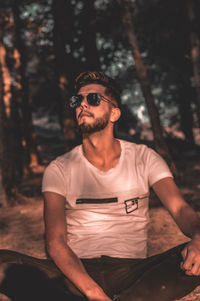 Young man wearing sunglasses standing against trees