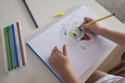 Cropped hands of child drawing in book