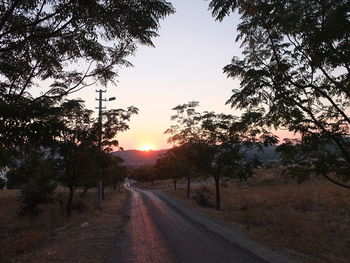 Road amidst trees against sky during sunset