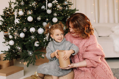 Happy mom and little daughter kid in sweaters hugging getting ready for  christmas holiday at home