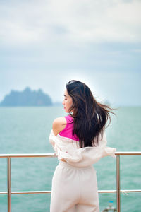 Young woman looking away while standing against sea