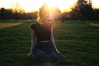Woman kneeling on field during sunset