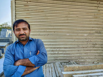 Portrait of a smiling young man standing against blue shutter