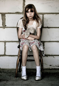 Portrait of girl holding stuffed toy and sitting on chair against wall