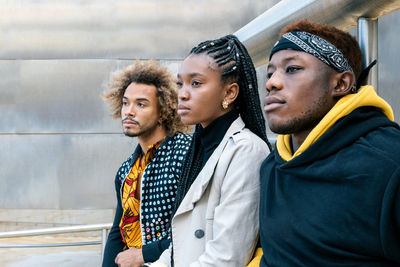 Serious unemotional young african american friends in casual informal clothes standing on stairway looking away while spending time together in city