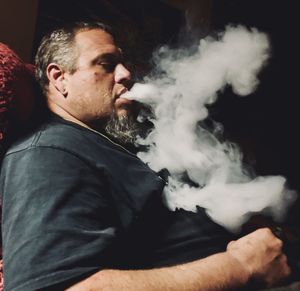 Young man smoking cigarette against black background