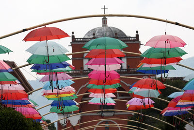 Low angle view of multi colored umbrellas hanging by building against sky