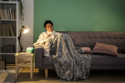 Mid adult woman knitting wool while sitting on sofa at home