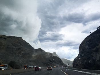 Road passing through mountains against cloudy sky