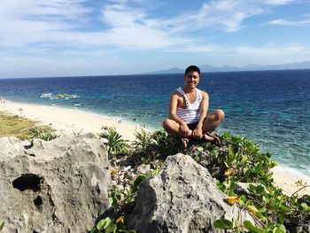 Portrait of man sitting on plants at beach against sky