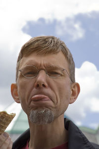 Portrait of mature man sticking out tongue against sky