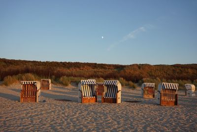 Hooded beach chairs on sand against blue sky during sunset