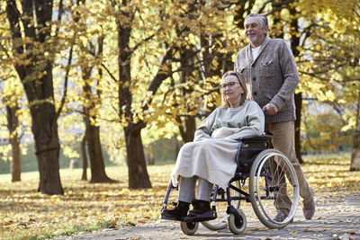 Senior man walking with disabled woman sitting in wheelchair at park