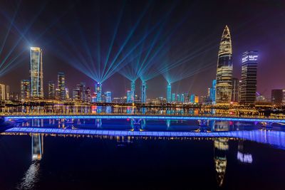 Illuminated bridge over river with buildings in background at night