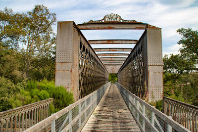 Footbridge amidst trees against sky