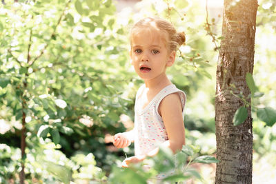 Portrait of cute girl standing by plants and trees in forest