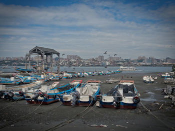 Sailboats moored on beach against sky in city