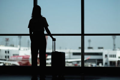 Rear view of silhouette woman standing at airport against sky