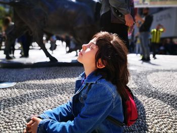 Girl sitting on footpath in city