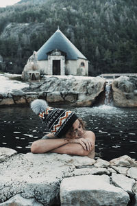 Rear view of woman sitting on rock by lake