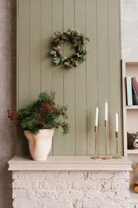 Christmas wreath of pine needles and cones hangs on the wall above the brick mantelpiece 