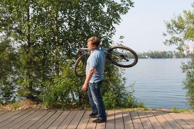 Frustrated man in the park carries broken bicycle on his shoulder.